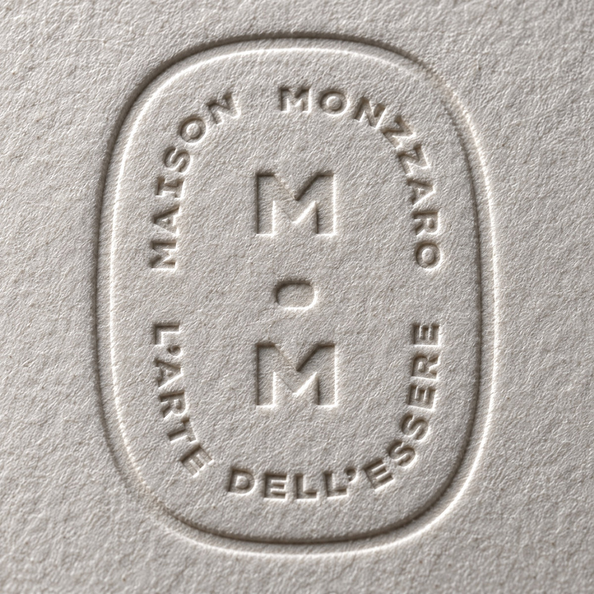 Close macro: the debossed house seal pressed into mono-cotton, raking light, no product